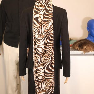 May include: A black blazer and skirt are displayed on a mannequin, complemented by a zebra-print scarf and head covering. Another mannequin wears a black shirt and white trousers. A blue head is also visible.