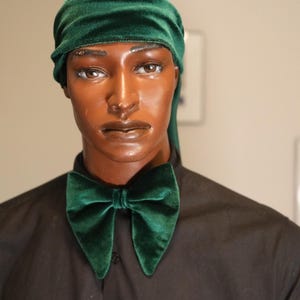 May include: A mannequin wearing a dark green velvet bow tie and matching head covering. The bow tie is a classic shape, and the head covering is a wrap style. The mannequin is wearing a black button-down shirt.