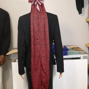 Puede incluir: Un maniquí viste un blazer y una falda negros. Un durag con estampado rojo y negro, con un diseño geométrico, está atado a la cabeza y cae por la espalda del maniquí.