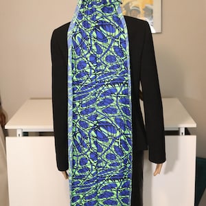 May include: A blue, green, and black patterned durag and scarf set. The fabric features a swirling design of blue and green lines on a black background. The scarf hangs down the back of a mannequin wearing a black blazer.