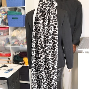May include: A black blazer with a long, leopard print scarf and matching head covering. The scarf and head covering feature a black and white spotted pattern. A mannequin is wearing the blazer and scarf.