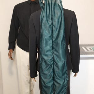 May include: A dark teal durag with a dotted pattern is draped over a mannequin wearing a black blazer. Another mannequin in a black shirt and white trousers stands in the background. The durag is the focal point.