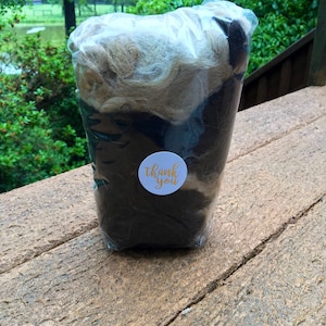 May include: A clear plastic bag filled with brown and light brown wool fibers. A white sticker with the text "thank you" in gold lettering is attached to the bag.