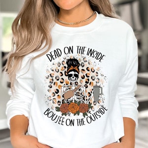 May include: White sweatshirt with a graphic of a skeleton woman with a leopard print background. The text on the sweatshirt reads "Dead on the inside, Boujee on the outside".