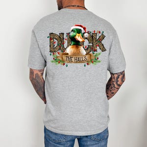 May include: A gray t-shirt with a Christmas-themed design featuring a duck wearing a Santa hat and the text "Duck the Halls" surrounded by greenery and Christmas lights.
