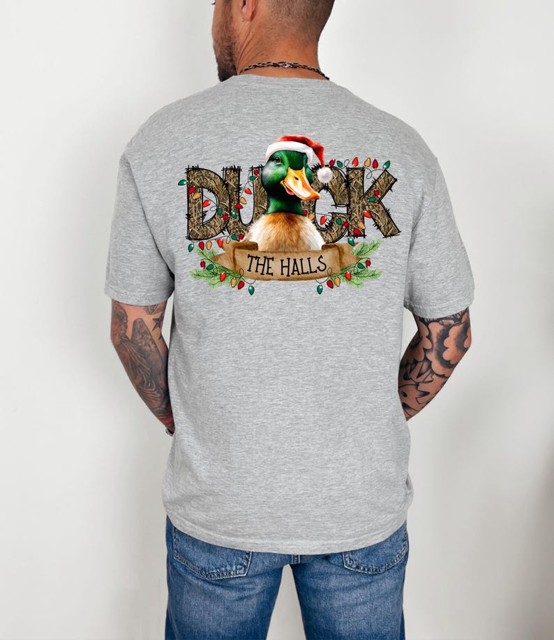 May include: A gray t-shirt with a Christmas-themed design featuring a duck wearing a Santa hat and the text "Duck the Halls" surrounded by greenery and Christmas lights.