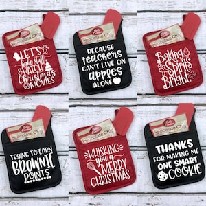 May include: Six red and black oven mitts with different Christmas-themed sayings. The mitts have a pocket on the back to hold a spatula and a small package of chocolate chips. The sayings on the mitts are: "Let's bake stuff & watch Christmas movies", "Because teachers can't live on apples alone", "Baking Spirits Bright", "Trying to earn brownie points", "Whisking you a Merry Christmas", and "Thanks for making me one smart cookie".