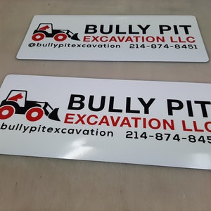 May include: White sign with black and red text and a black and red illustration of a bulldozer. The text reads "Bully Pit Excavation LLC" and includes the phone number "214-874-8451" and the social media handle "@bullypitexcavation".