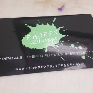 May include: Black and green business card with a green splatter paint design and the text "The Proppy Shoppe" in white. The text "Prop Rentals Themed Florals & Stylized Events" and "www.theproppyshoppe.com" are also in white.