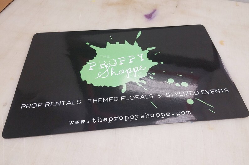 May include: Black and green business card with a green splatter paint design and the text "The Proppy Shoppe" in white. The text "Prop Rentals Themed Florals & Stylized Events" and "www.theproppyshoppe.com" are also in white.