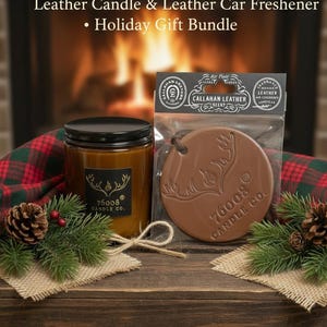 May include: A holiday gift bundle featuring a leather-scented candle and car freshener. The candle is in a glass jar with a black lid and a label that reads "76008 CANDLE CO." The car freshener is a brown, circular shape with a deer design and the text "CALLAHAN LEATHER".