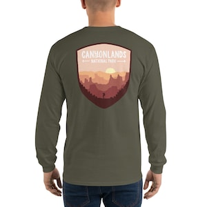 May include: A green long-sleeve t-shirt with a graphic of a shield featuring a sunset landscape and the text "Canyonlands National Park".