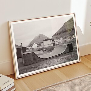 May include: Black and white photograph of a half-pipe skate ramp in a small town with a mountain in the background.