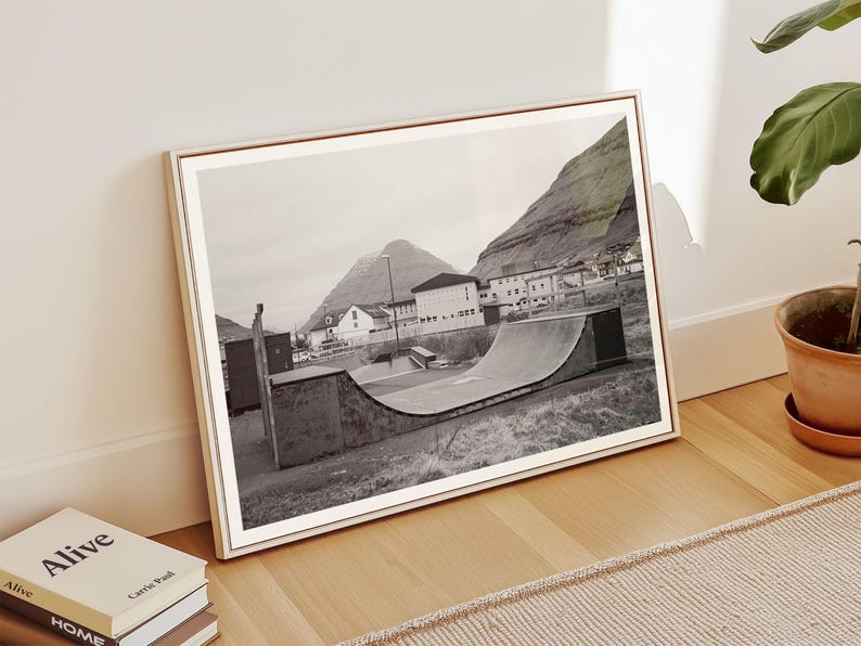 May include: Black and white photograph of a half-pipe skate ramp in a small town with a mountain in the background.