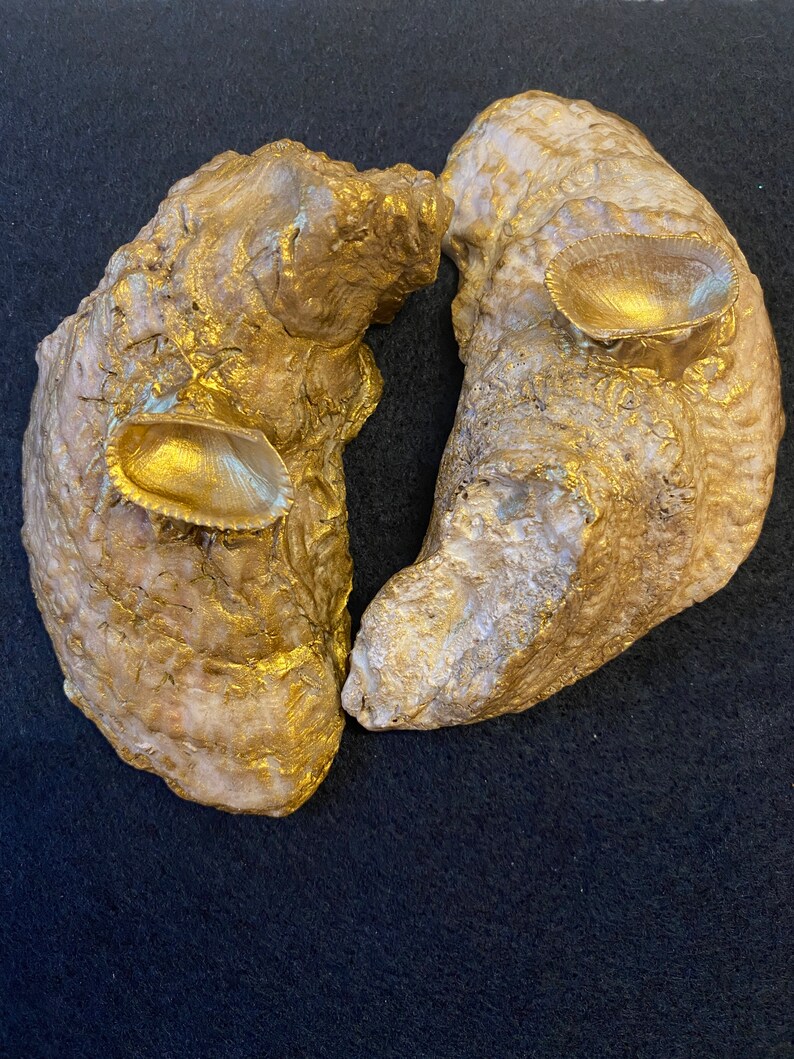 May include: Two golden, organic, freeform shapes with a textured surface. Each shape has a small, golden, circular indentation.