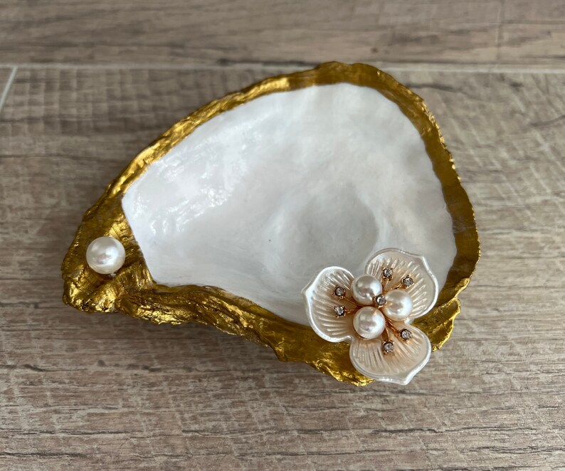 May include: A white oyster shell dish with gold accents, featuring a pearl and a white flower with pearl and rhinestone embellishments.