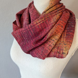May include: A red, orange, and yellow infinity scarf made of woven fabric. The scarf is draped around a white mannequin.