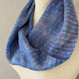 Puede incluir: Bufanda infinita azul y morada sobre un maniqu&iacute;. La bufanda es de tejido con aspecto texturizado. La paleta de colores incluye tonos de azul, morado y blanco. La bufanda es un bucle continuo, dise&ntilde;ada para llevar alrededor del cuello.