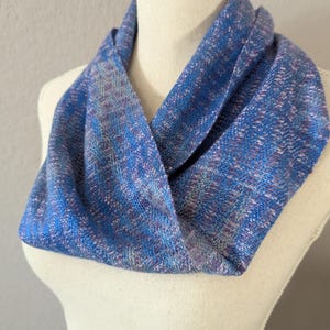 Puede incluir: Un pa&ntilde;uelo infinito azul con una textura tejida, exhibido en un maniqu&iacute;. El pa&ntilde;uelo presenta tonos de azul, morado y blanco, creando un patr&oacute;n texturizado. Este accesorio es una adici&oacute;n elegante a cualquier guardarropa.