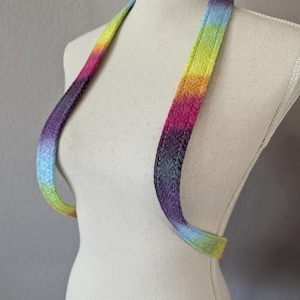 May include: A rainbow-hued halter top with a woven texture. The straps display a gradient of colours, including blue, purple, pink, orange, and yellow. The halter is shown on a mannequin.