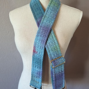 May include: A blue and purple patterned adjustable strap with a gold metal buckle and black metal clips. The strap is made of woven fabric and is suitable for bags or purses.