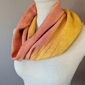 May include: A yellow and pink striped infinity scarf made of woven fabric.