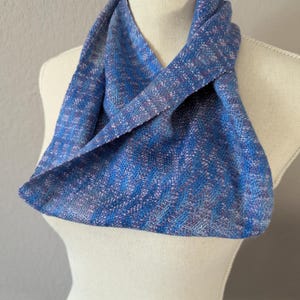 Puede incluir: Bufanda infinita azul con un patr&oacute;n tejido. La bufanda se muestra en un maniqu&iacute; y presenta tonos de azul, morado y blanco. La tela parece suave y ligera, adecuada para climas m&aacute;s frescos. Un accesorio vers&aacute;til.