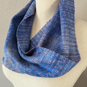 Puede incluir: Un pa&ntilde;uelo infinito azul con una textura tejida. El pa&ntilde;uelo presenta tonos de azul, con toques de morado y blanco. El pa&ntilde;uelo est&aacute; drapeado sobre un maniqu&iacute;, mostrando su dise&ntilde;o circular y su apariencia suave.