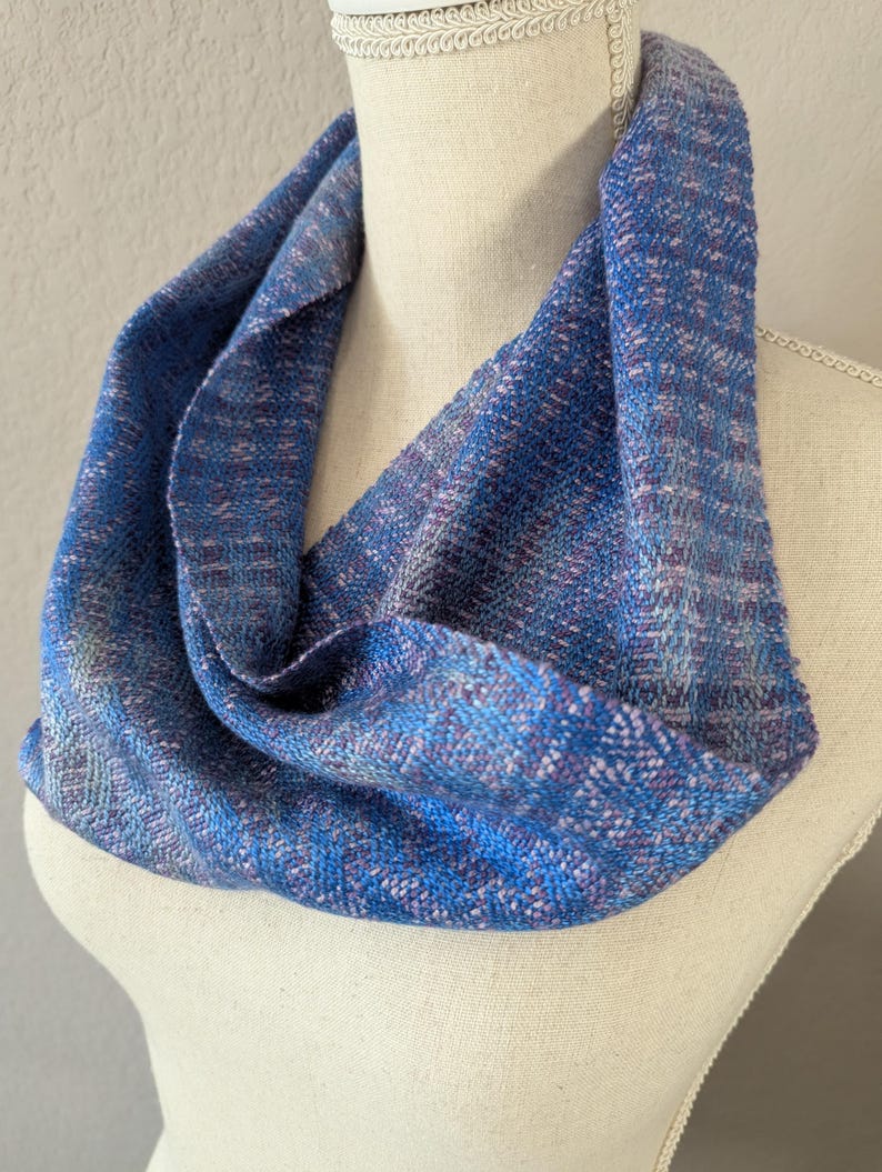 Puede incluir: Un pa&ntilde;uelo infinito azul con una textura tejida. El pa&ntilde;uelo presenta tonos de azul, con toques de morado y blanco. El pa&ntilde;uelo est&aacute; drapeado sobre un maniqu&iacute;, mostrando su dise&ntilde;o circular y su apariencia suave.