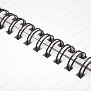 May include: Close-up of a black wire binding on a white lined notebook.