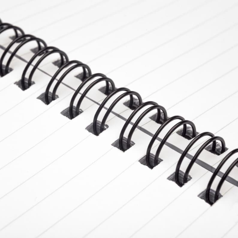 May include: Close-up of a black wire binding on a white lined notebook.