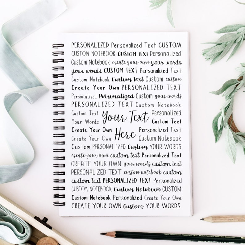 May include: A white notebook with a black spiral binding. The notebook has a variety of text printed on the cover, including "Personalized Text", "Custom Notebook", "Create Your Own", and "Your Text".