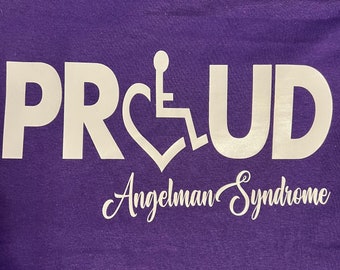 May include: Purple t-shirt with white text that reads "PRUD" with a stylized wheelchair symbol in the middle of the word. The text "Angelman Syndrome" is written in cursive below the word "PRUD".
