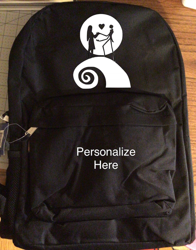 May include: Black backpack with a white design of a couple standing on a hill with a heart above them. The hill is shaped like a spiral. The text "Personalize Here" is printed on the front of the backpack.