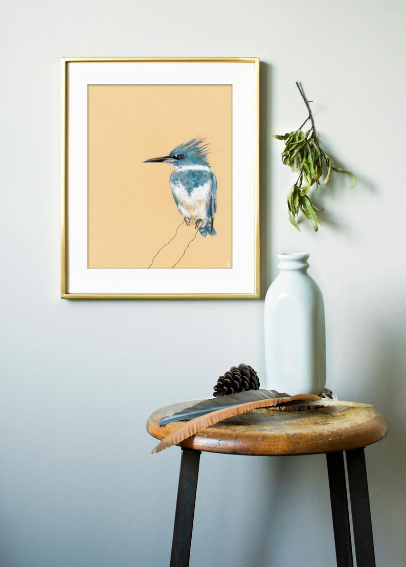 May include: A framed print of a blue and white bird with a long beak, perched on a branch. The print is on a light beige background and is framed in gold.