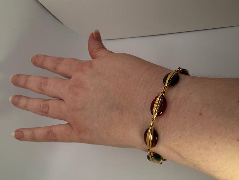 Puede incluir: Pulsera dorada con cuentas ovaladas rojas, verdes y negras. Las cuentas est&aacute;n engarzadas en metal dorado y unidas por una fina cadena. Un accesorio elegante para cualquier ocasi&oacute;n.