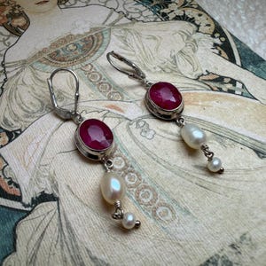 Peut inclure: Une paire de boucles d'oreilles pendantes en argent avec des pierres rubis rose foncé à facettes de forme ovale serties dans des chatons en métal, chacune ornée de deux perles d'eau douce blanches de tailles différentes et d'un fermoir dormeuse.