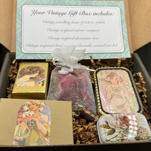 May include: A vintage gift box filled with various items. Includes vintage jewelry, a mirror compact, a decorative box, and a sachet. The box contains a gold-colored box with a woman's portrait, a small bag of dried flowers, and a decorative tin.