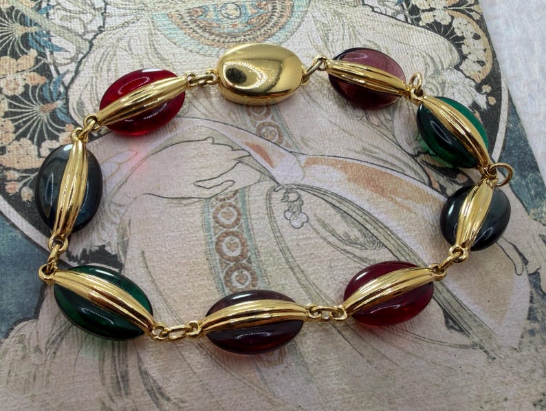 Puede incluir: Un collar dorado con cuentas ovaladas en rojo, verde, negro y morado. Las cuentas est&aacute;n unidas por eslabones dorados. El collar tiene un estilo vintage.
