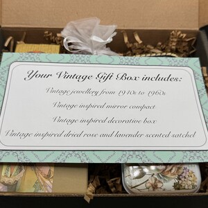 May include: A vintage gift box, open to reveal contents. A card reads "Your Vintage Gift Box includes: Vintage jewellery from 1910s to 1960s, Vintage inspired mirror compact, Vintage inspired decorative box, Vintage inspired dried rose and lavender scented satchel."