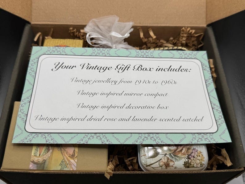 May include: A vintage gift box, open to reveal contents. A card reads "Your Vintage Gift Box includes: Vintage jewellery from 1910s to 1960s, Vintage inspired mirror compact, Vintage inspired decorative box, Vintage inspired dried rose and lavender scented satchel."
