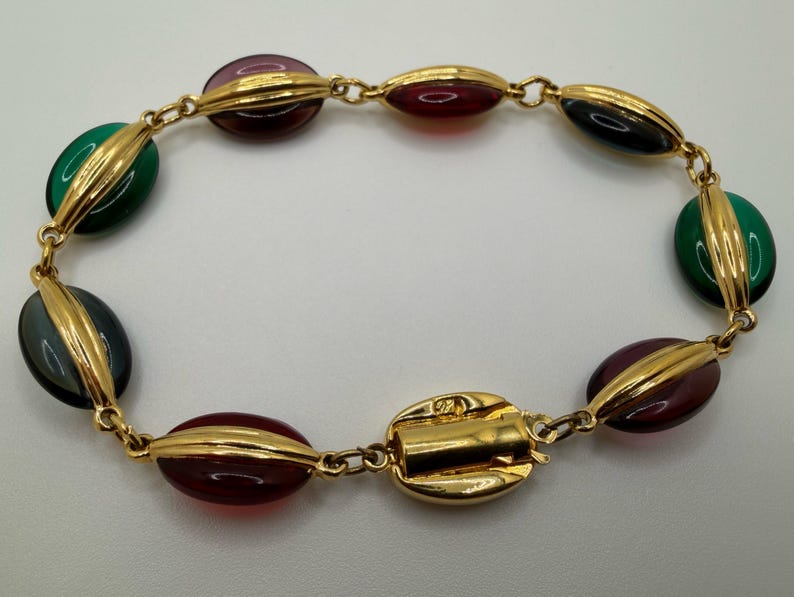 Puede incluir: Una pulsera dorada con cuentas ovaladas en tonos verdes, burdeos y negro. Las cuentas est&aacute;n separadas por detalles dorados y unidas por una delicada cadena. El cierre tambi&eacute;n es dorado.