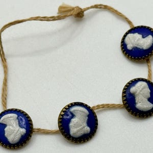 May include: Four blue and white cameo buttons with gold trim are strung on a length of twine.