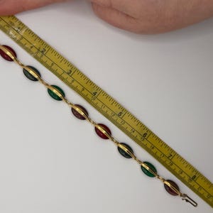 Puede incluir: Pulsera dorada con piedras ovaladas rojas, verdes y verde oscuro alternadas. La pulsera mide aproximadamente 20 cm de largo y tiene un cierre de broche. Las piedras est&aacute;n engastadas en metal dorado.