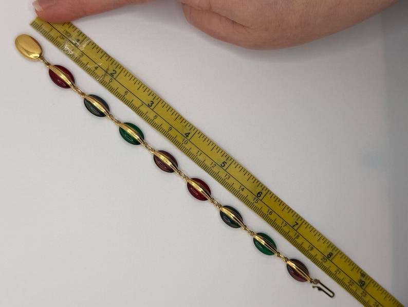 Puede incluir: Pulsera dorada con piedras ovaladas rojas, verdes y verde oscuro alternadas. La pulsera mide aproximadamente 20 cm de largo y tiene un cierre de broche. Las piedras est&aacute;n engastadas en metal dorado.