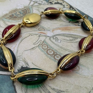 Puede incluir: Un brazalete vintage con cuentas ovaladas en dorado, rojo, verde y azul oscuro. Las cuentas est&aacute;n unidas por eslabones de metal dorado. El brazalete tiene un dise&ntilde;o cl&aacute;sico y elegante, ideal para a&ntilde;adir un toque vintage a cualquier atuendo.