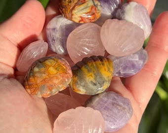 May include: A collection of polished gemstones in various shapes and colors. The assortment includes rose quartz, amethyst, and uniquely patterned stones in shades of yellow, orange, and gray. The gemstones are held in a hand, showcasing their natural beauty.