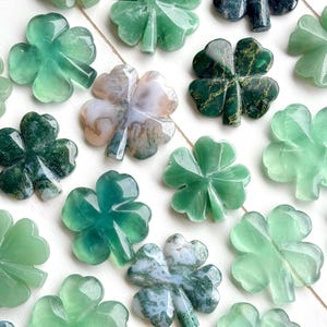 May include: A collection of green four-leaf clover charms carved from agate. The charms have different patterns and shades of green.