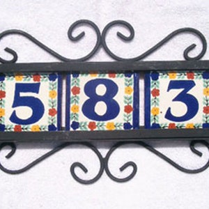May include: Decorative address plaque featuring the numbers "583" on three ceramic tiles. The tiles have a floral design with blue, red, and yellow accents. The plaque is framed by a black wrought iron scroll design.