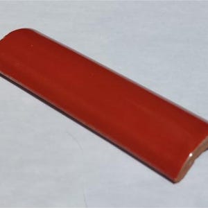 May include: A red ceramic tile trim piece with a rounded edge. The tile is glazed and has a smooth finish.